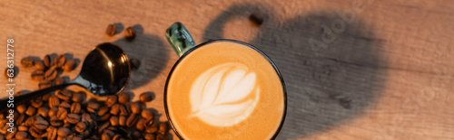 top view of cup of cappuccino near coffee beans and spoon on table in cafe  banner