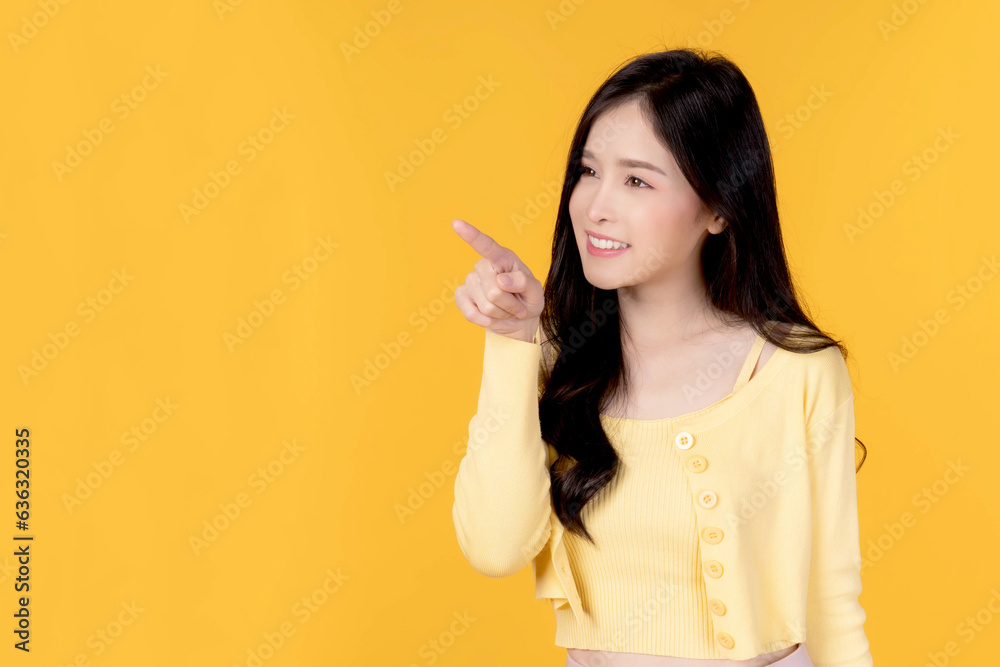 Beautiful Asian woman cute girl in with yellow shirt smiling and pointing finger to empty copy space for present product or blank space for advertising isolated on yellow background Beautiful Asian woman cute girl in with yellow shirt smiling and pointing finger to empty copy space for present product or blank space for advertising isolated on yellow background