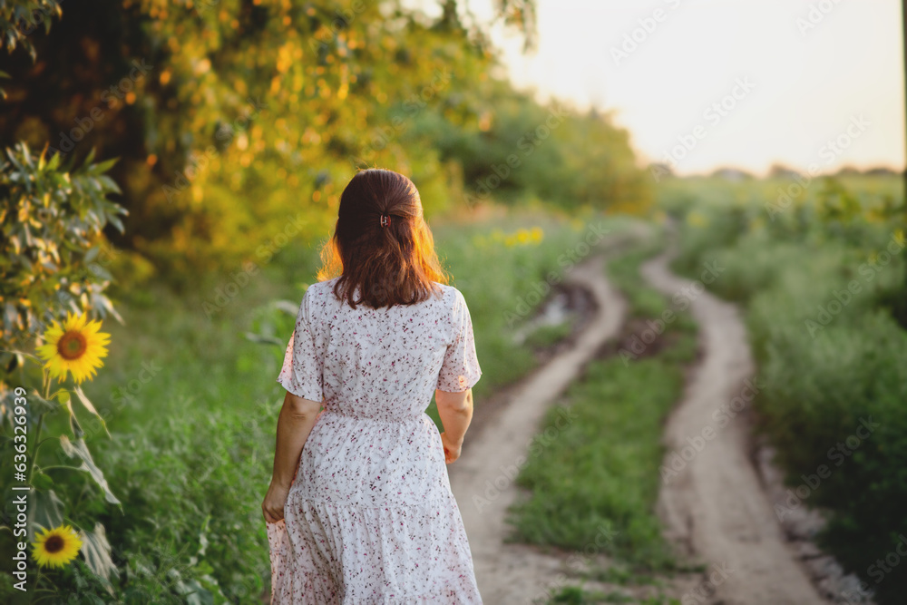 romantic young woman walks on field in nature, view of a girl in a summer dress from the back romantic young woman walks on field in nature, view of a girl in a summer dress from the back