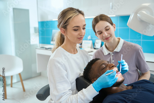 Young nurse assisting to woman dentist during patient oral cavity checkup