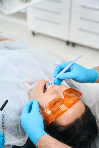 Dentist in dental office puts photopolymer filling on brunette woman