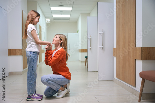 Female in an orange sweater holds the girls hand in the clinic