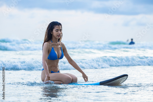 Asian female surfer in swimsuit holding a surfboard