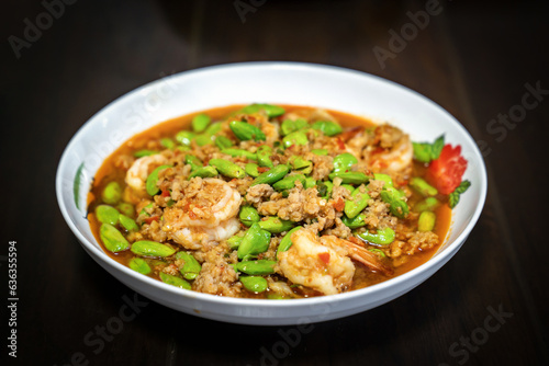 Thai Stir-Fried Stink Beans with Shrimps and spicy shrimp paste sauce in white dish bowl on dark wood table. Clipping Path.