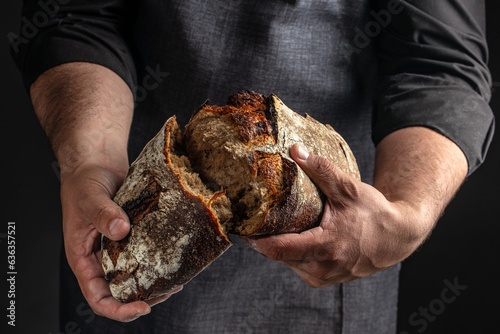 man breaking fresh bread on a dark background. banner, menu, recipe place for text, top view