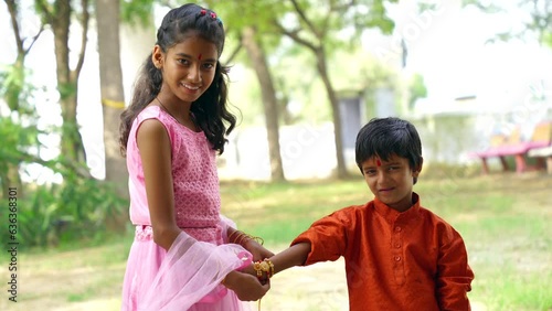 Cute little Indian Sister tying Rakhi to Her little brother's wrist and exchanging gifts and sweets on Raksha Bandhan or Bhai Dooj festival photo