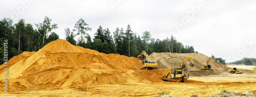 a crawler excavator loads sand into a truck. Large hills and heaps of sand, gravel, crushed stone of yellow, gray and black colors