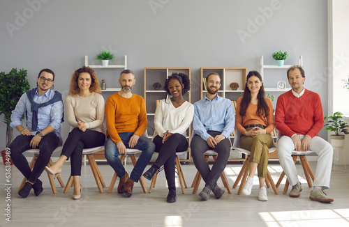 Happy smiling male and female audience sitting on row of chairs in modern cozy office room. Diverse group of positive young and old people enjoying interesting business event or club meeting