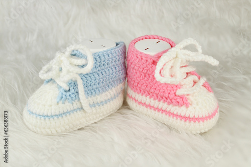Knitted pink and blue booties on white fluffy blanket. Gender party concept idea. Booties for baby girl or boy for first step. 