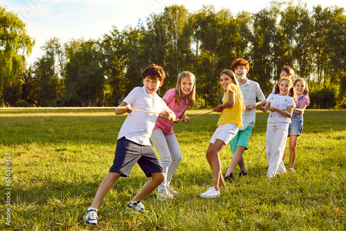 Happy kids playing games and having fun in summer camp on vacation. Team of children playing tug of war, standing on green field and pulling rope all together. Summer, fun, activity, teamwork concept