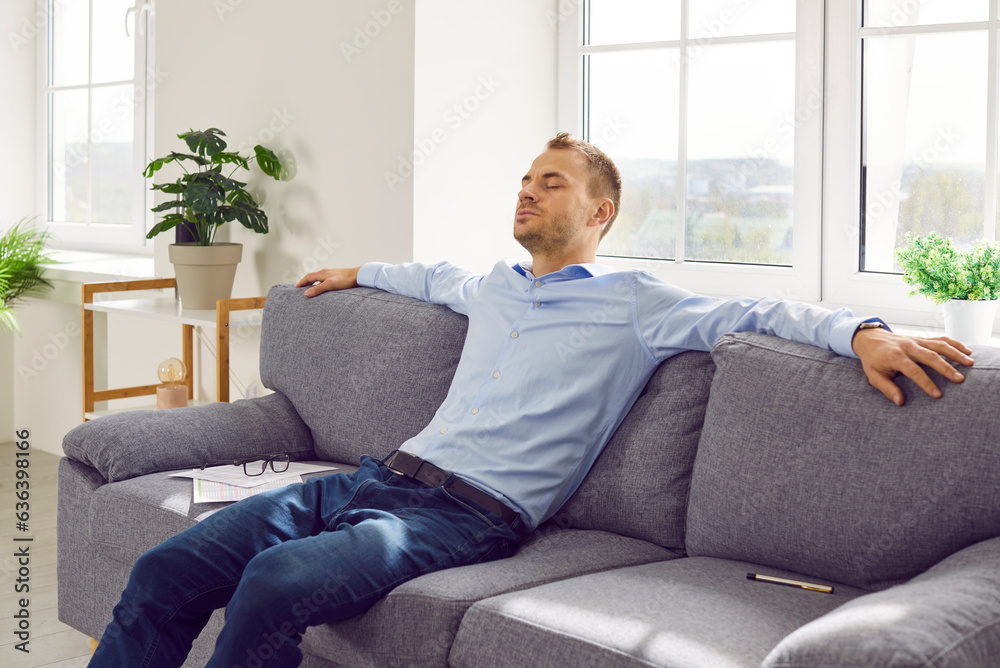 Young businessman relaxing on couch at home. Calm, relaxed business man having weekend or taking break during work, sitting on sofa, and enjoying free time. Concept of rest, relaxation, pause, break