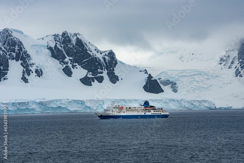 Large sailboat pictured in front of a stunning backdrop of snowy mountainous terrain in Antarctica