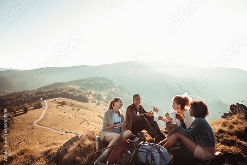 Young diverse group of female friends having a coffee break after hiking in the hills and mountains photo