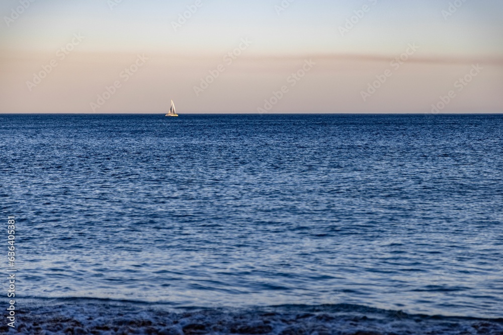 Scenic view of a sailboat gliding across a tranquil sea at sunset