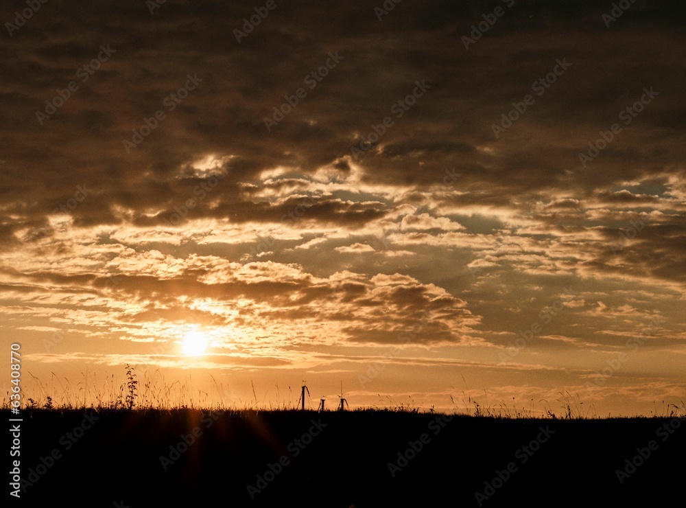 Mesmerizing orange sunset over the silhouette of a field under the cloudy sky