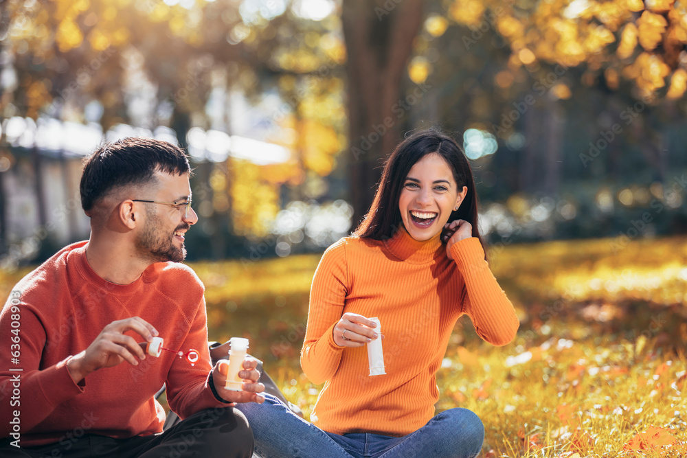 Couple blowing bubbles and having a fun time. Sunny autumn day in the colorful park Couple blowing bubbles and having a fun time. Sunny autumn day in the colorful park