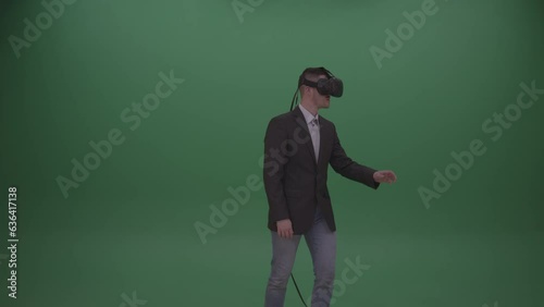 Young Black-Haired Male Wearing Dark Brown Jacket, White Shirt, Exploring Virtual Environment Using VR Glasses, Green Screen Wall Background (ID: 636417138)