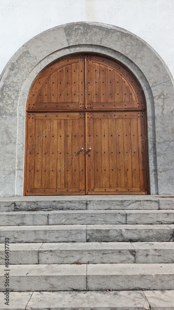 A large wide door made of boards, the entrance to the church, a wide staircase made of stone and a white wall
