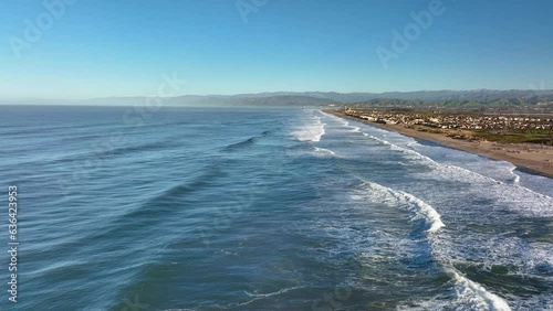 Aerial view of ocean waves crashing against sandy beach with coastal houses in Ventura, California