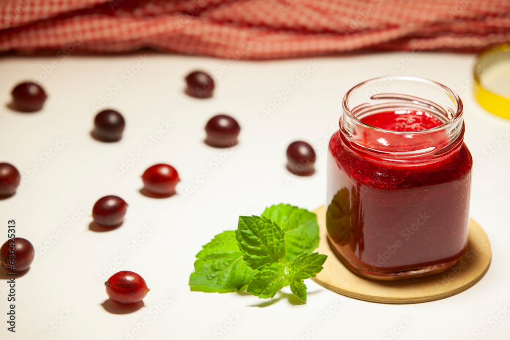 A jar of delicious gooseberry jam, fresh berries and sprig of mint on a white background. Selective focus, close-up.