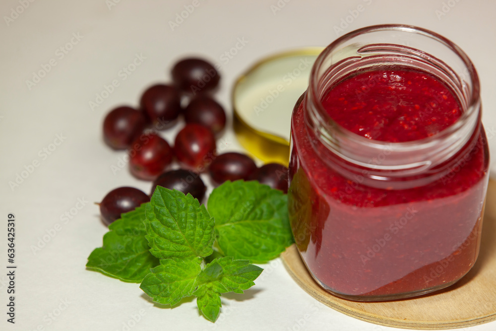 A jar of delicious gooseberry jam, fresh berries and sprig of mint on a white background, close-up.
