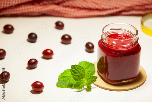 Obraz na płótnie A jar of delicious gooseberry jam, fresh berries and sprig of mint on a white background. Selective focus, close-up. w salonie
