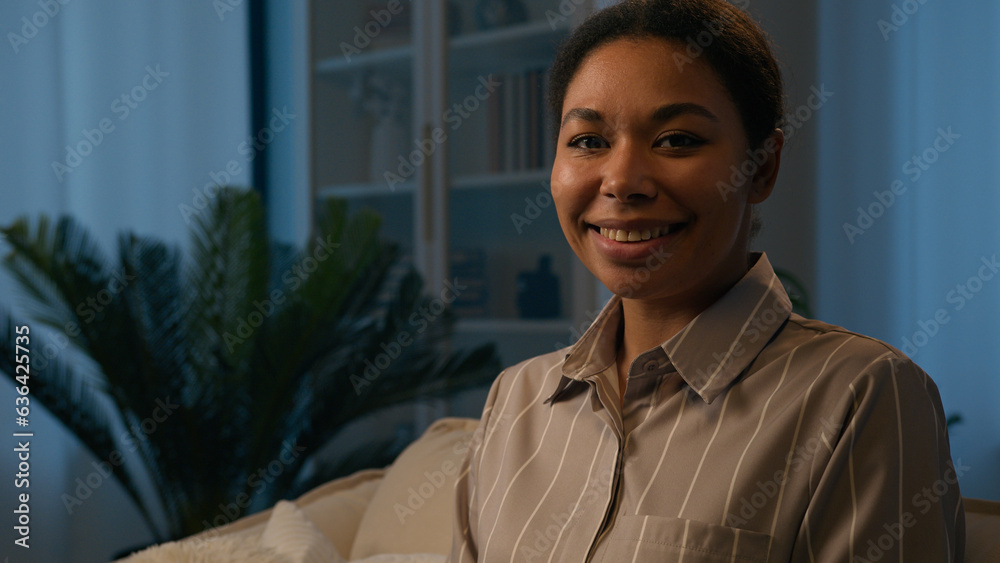 Female portrait ethnic woman African American girl on comfort couch in evening night home happy lady homeowner girlfriend wife mother owner of apartment estate looking at camera cheerful toothy smile Female portrait ethnic woman African American girl on comfort couch in evening night home happy lady homeowner girlfriend wife mother owner of apartment estate looking at camera cheerful toothy smile