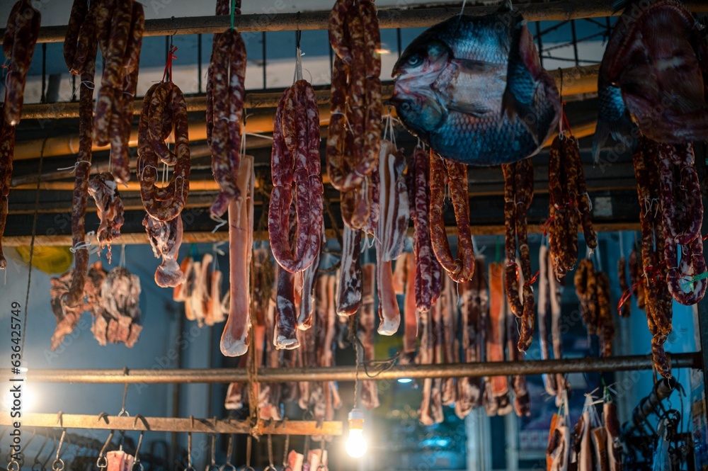 Busy market, showing a variety of preserved sausages hanging from a large industrial roof