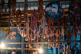 Busy market, showing a variety of preserved sausages hanging from a large industrial roof