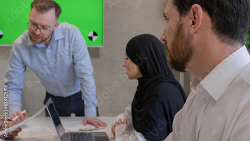 Multiethnic colleagues businessmen and muslim businesswoman in hijab teamwork in office boardroom business team talk brainstorming discussion with green screen interactive board copy space chroma key