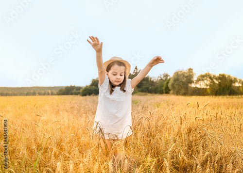 Happy girl walks in beautiful wheat field, embracing summer's yellow sun, nature freedom outdoors. White dress, straw hat, surrounded by rye, barley. Autumn harvest time rural scene.Own piece of land