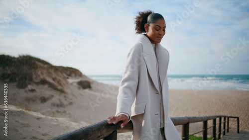 Black hair woman lean railings at ocean beach. Serene traveler resting shore