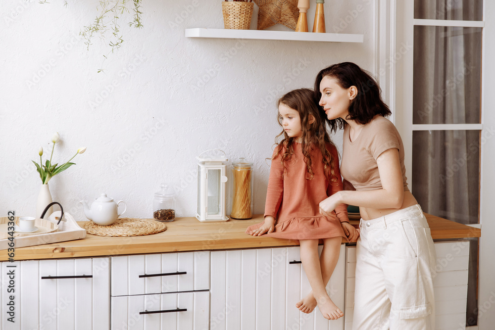 Mom and little daughter in a beautiful stylish kitchen in a modern design look at the copy space. The concept of a catalog or advertisement of furniture or maternity. Mom and little daughter in a beautiful stylish kitchen in a modern design look at the copy space. The concept of a catalog or advertisement of furniture or maternity.