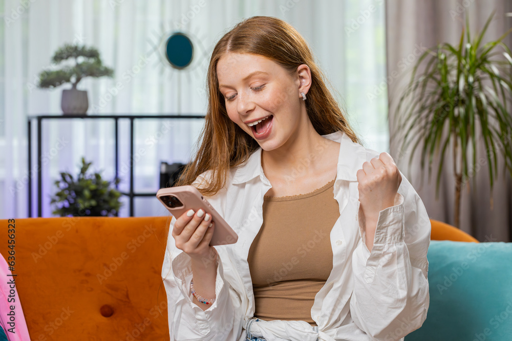 Happy teenager girl use mobile smartphone typing browsing say Wow yes found out great big win good news celebrate lottery jackpot, play victory game. Portrait of child at home in room sitting on sofa Happy teenager girl use mobile smartphone typing browsing say Wow yes found out great big win good news celebrate lottery jackpot, play victory game. Portrait of child at home in room sitting on sofa