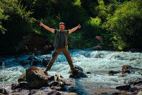 Happy hiker with trekking poles stands in the middle of a rushing mountain river