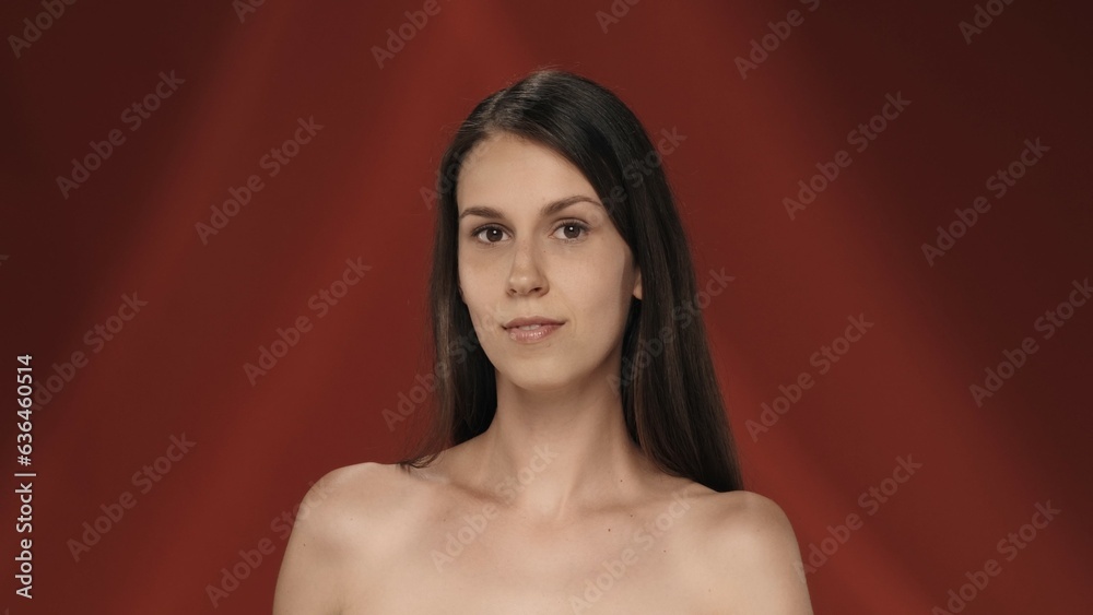Portrait of a young longhaired seminude woman in the studio on a red background. The concept of beauty, cosmetology, care and women's health. Portrait of a young longhaired seminude woman in the studio on a red background. The concept of beauty, cosmetology, care and women's health.