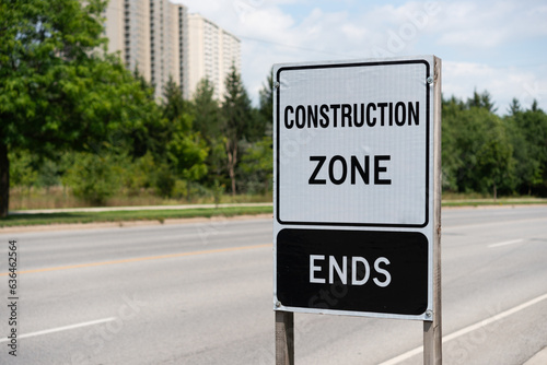 Construction Zone Ends sign with view of road and woodlot and architecture in the distance © eugen
