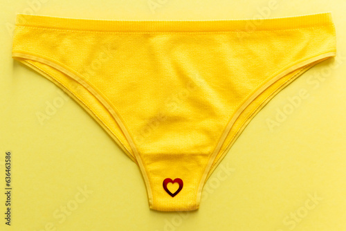 Top view of colorful females panties with red heart confetti on yellow background