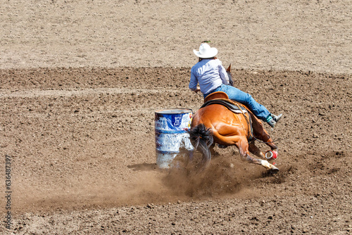 A cowgirl is riding a horse in a rodeo. She is competing in a barrel racing contest. The horse is kicking up a lot of dirt rounding the barrel. The horse is brown and the cowgirl is wearing blue.