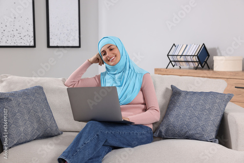 Muslim woman using laptop at couch in room