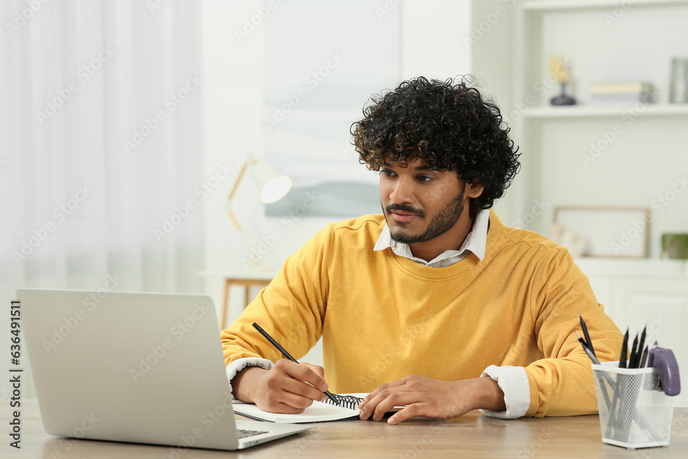 Handsome man taking notes near laptop in room