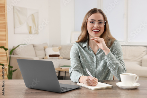 Happy woman with notebook and laptop at wooden table in room © New Africa