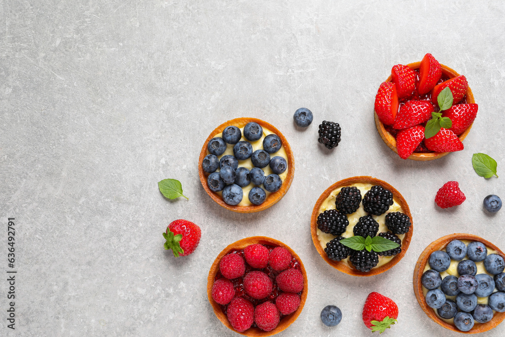Tartlets with different fresh berries on light grey table, flat lay and space for text. Delicious dessert