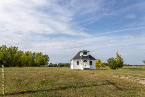 Sunny landscape view of a rural 19th century wood constructed one-room country schoolhouse on a prairie in midwestern USA  with blue sky background.