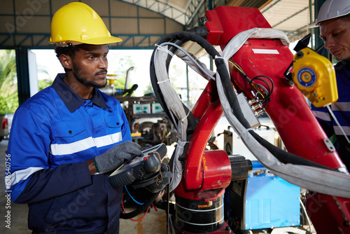 African factory workers or engineer operating remote switch controller to control robot machine in the factory