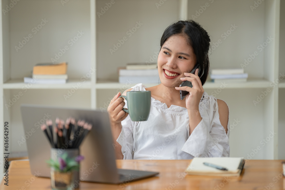 A young Asian businesswoman talking on her mobile phone while sitting at her working place in the office. A young Asian businesswoman talking on her mobile phone while sitting at her working place in the office.