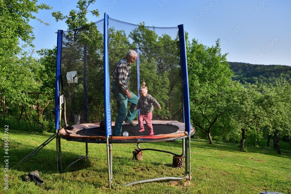 Grandfather and his granddaughter are playing on the trampoline