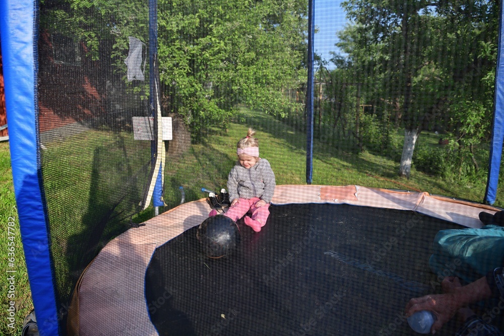 A little girl runs around in a trampoline and kicks a ball with her grandfather