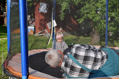 Obraz na płótnie A little girl runs around in a trampoline and kicks a ball with her grandfather w salonie
