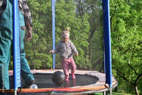 Obraz na płótnie A 2-year-old girl jumps and kicks a ball on a trampoline in the summer w salonie